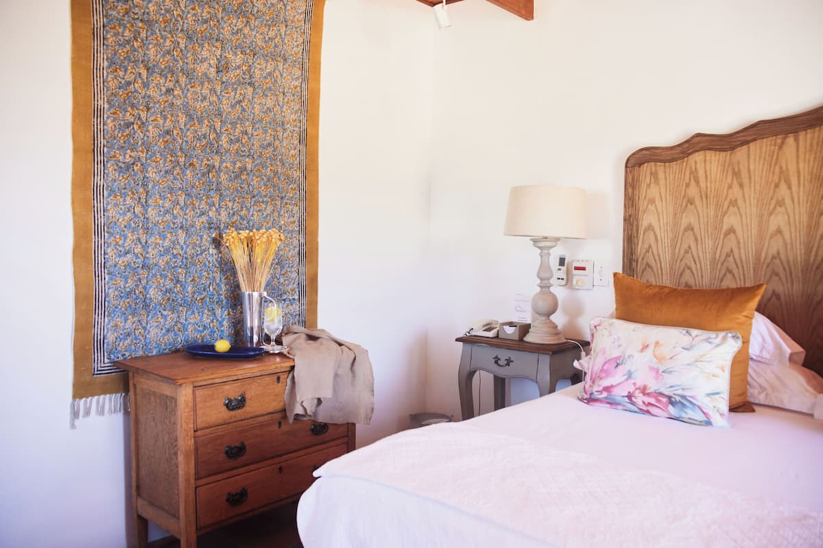 A bedroom with a wooden headboard, a bedside table with a lamp, a nightstand, and a dresser with drawers.