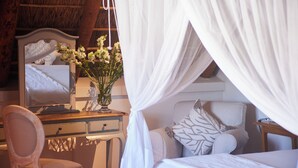 A bedroom with a bed, a bedside table with a mirror, a chair, and a desk. - Klein Waterval Riverside Lodge (Franschhoek)