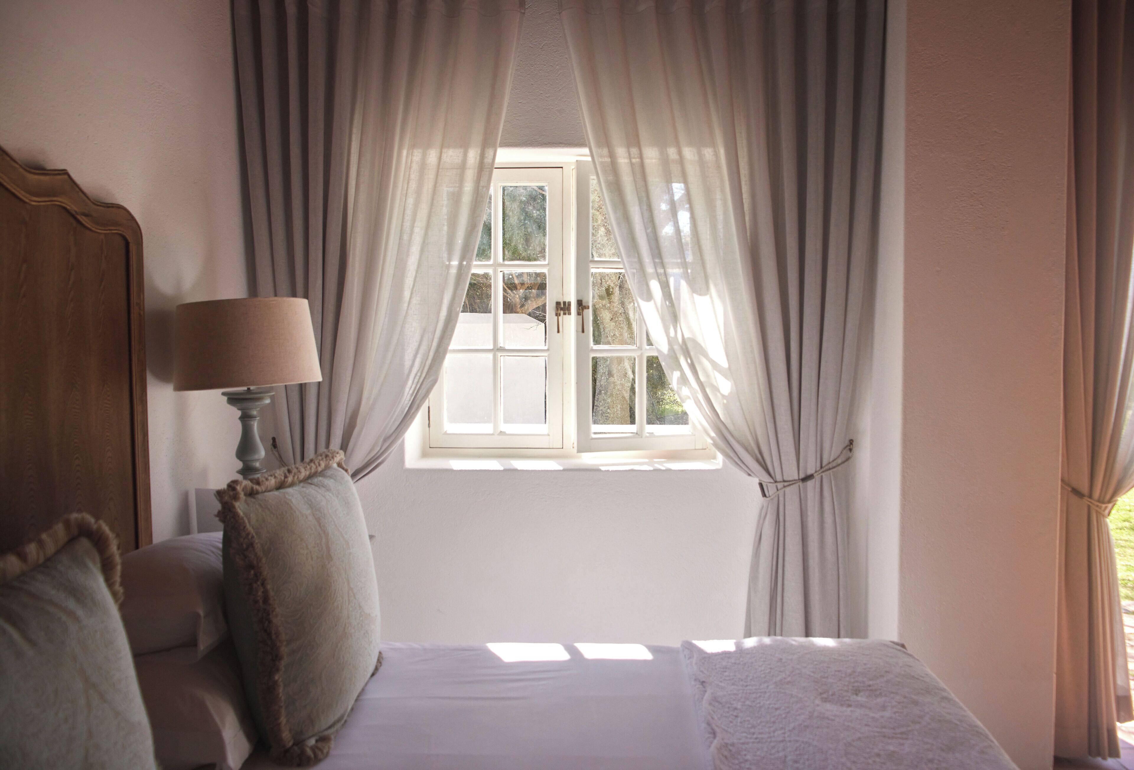 A bedroom with a bed, a bedside table with a lamp, and a window with curtains.