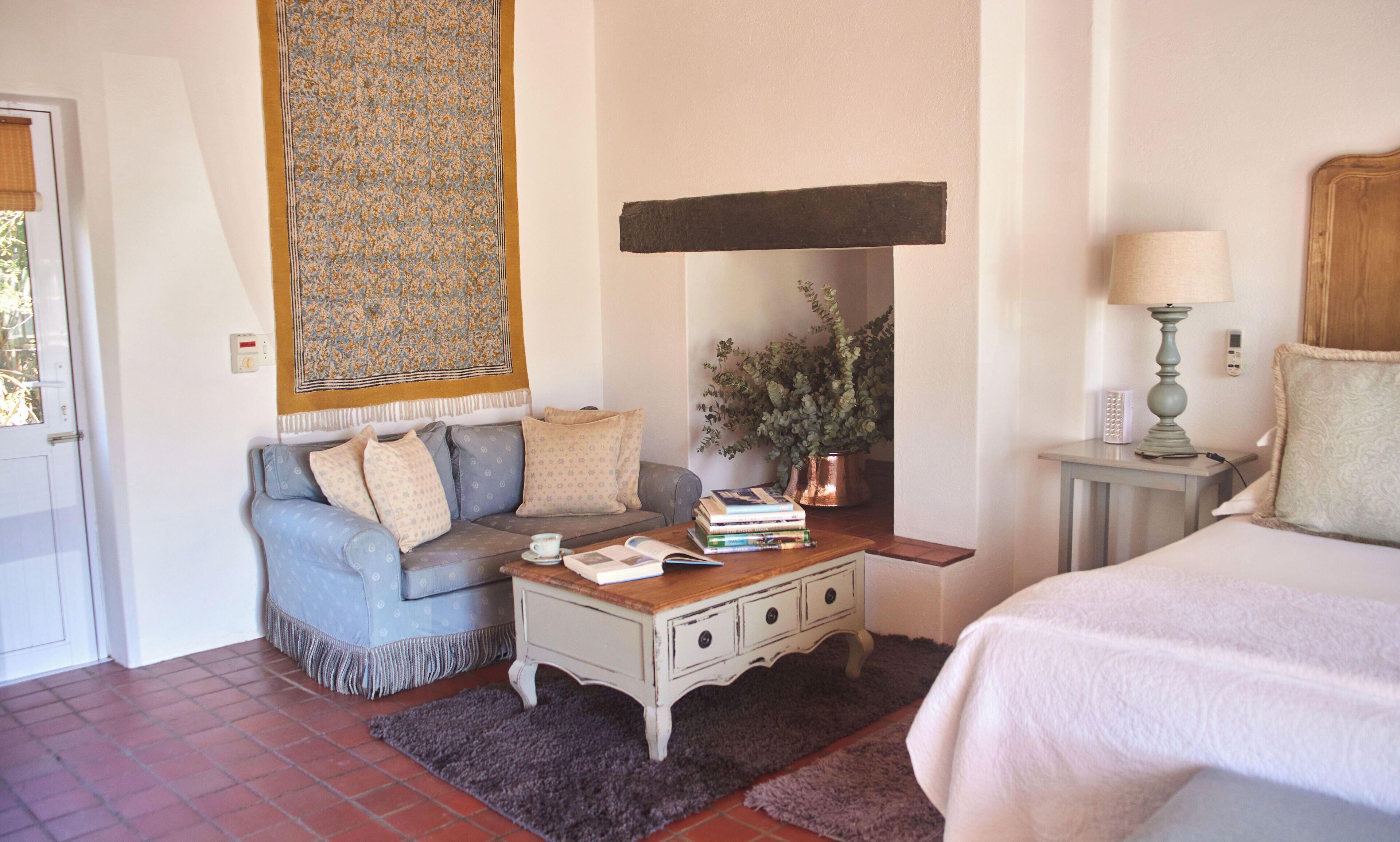 Un dormitorio con cama, sofá, una mesita de centro con libros, mesita de noche con lámpara y un calentador de pared.
