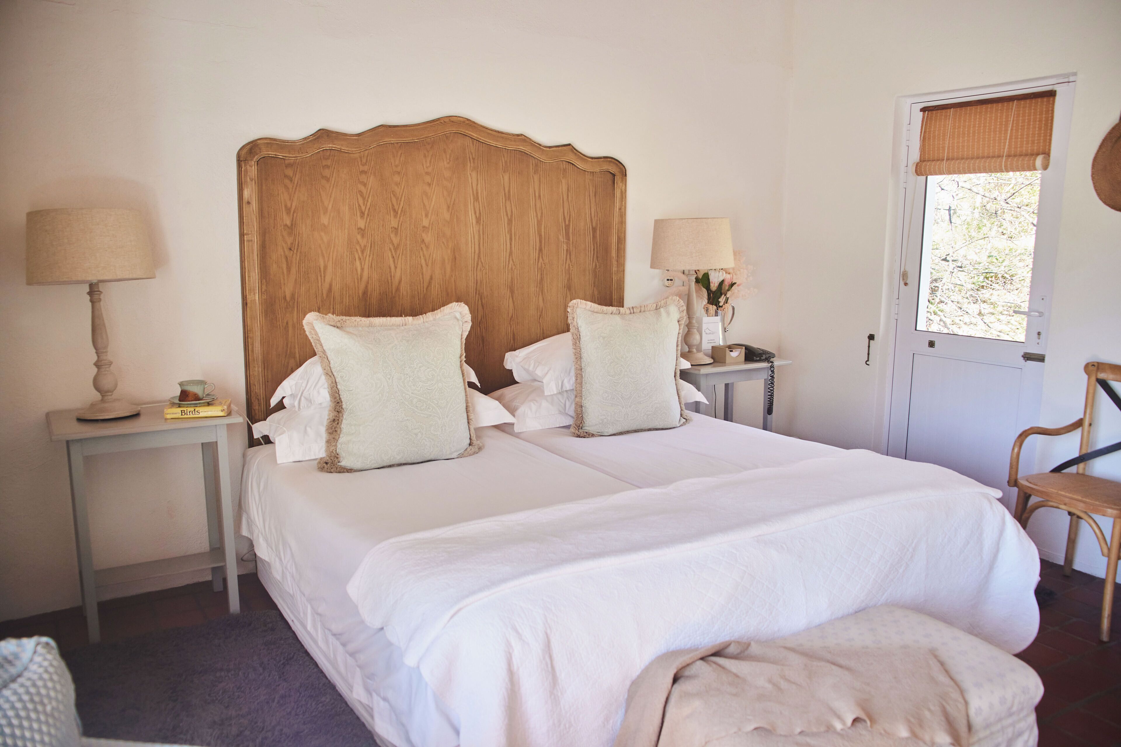 Una cama doble con cabecera de madera, dos mesitas de noche con lámparas, una silla y una puerta con ventana.