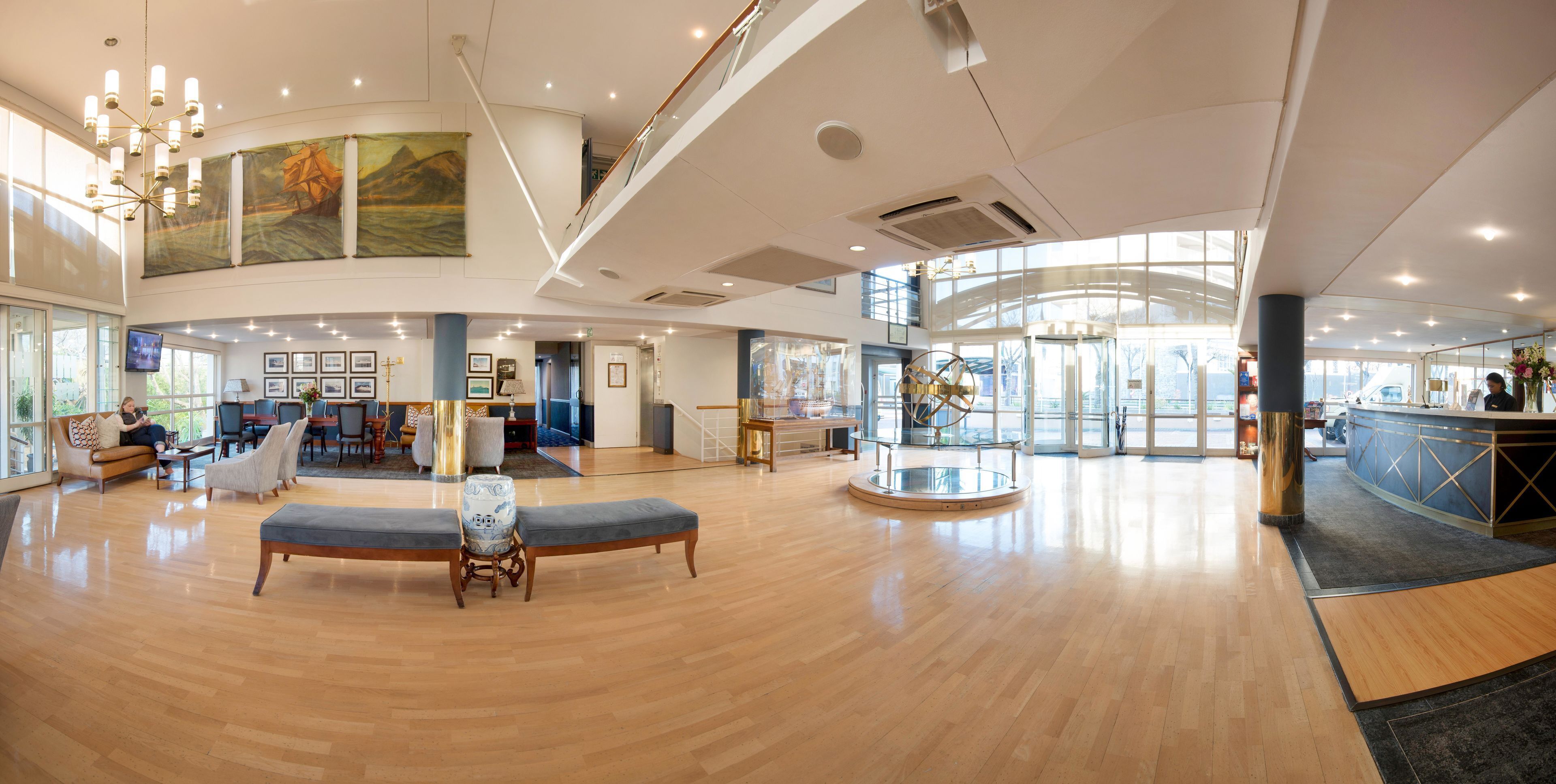 Un'ampia hall con pavimento in legno, zone relax, una reception e un'ampia vetrata che illumina naturalmente l'ambiente.