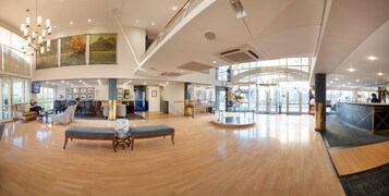 Un hall d’entrée spacieux doté d’un plancher en bois, de coins salon, d’un comptoir d’accueil et d’une grande fenêtre laissant entrer la lumière naturelle.