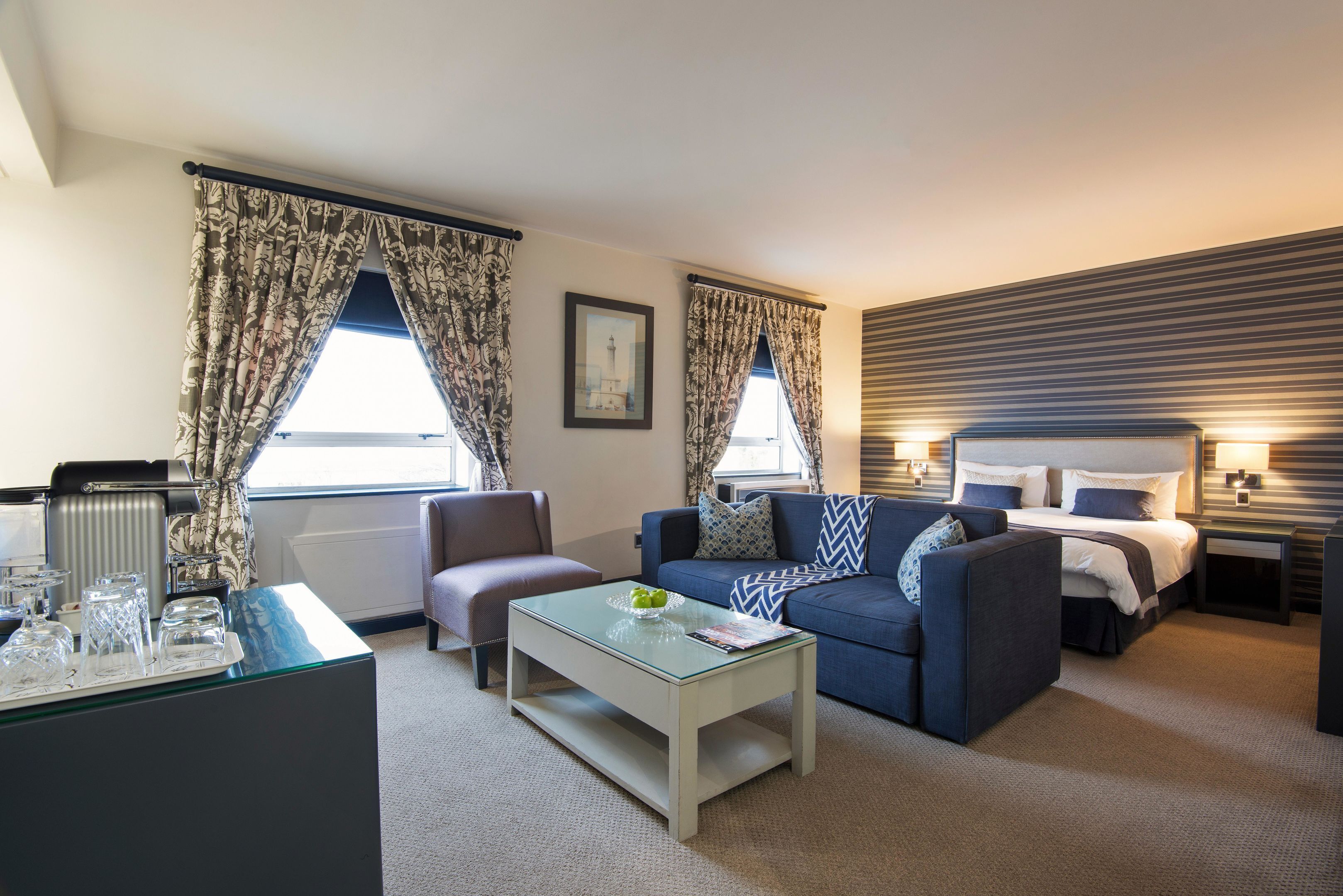 Quarto de hotel moderno com sofá, mesa de centro, cama e escrivaninha com luminária.