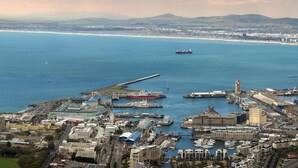 An aerial view of a coastal city with a marina, industrial buildings, and a large ship docked at the port. - The Portswood Hotel (Cape Town)