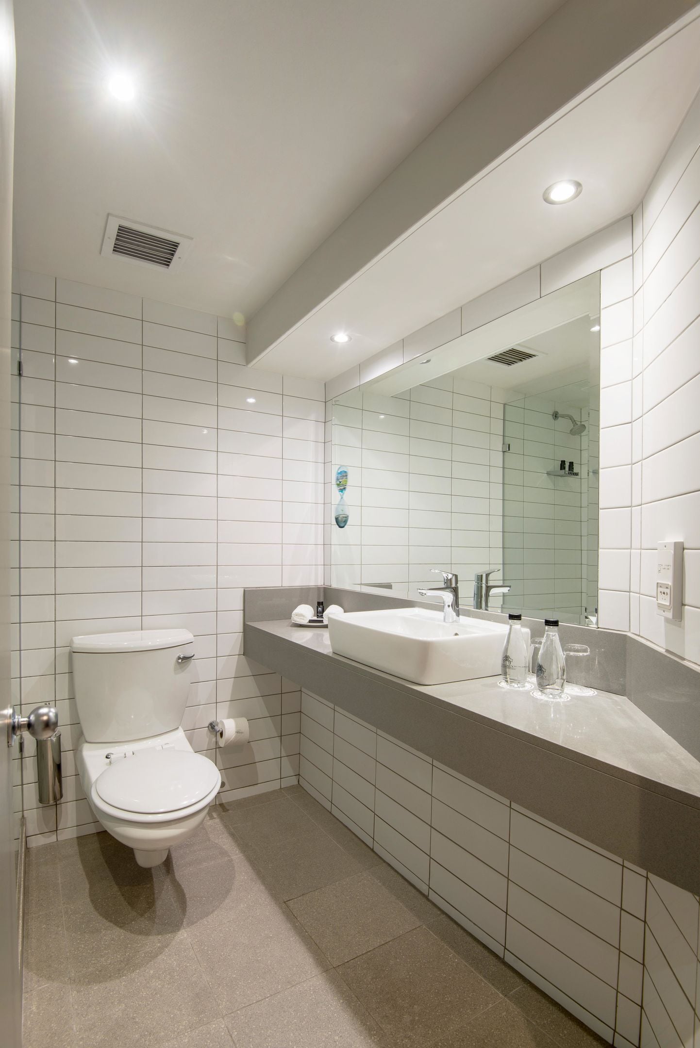A modern bathroom with a white toilet, a large mirror, and a sink with a countertop.