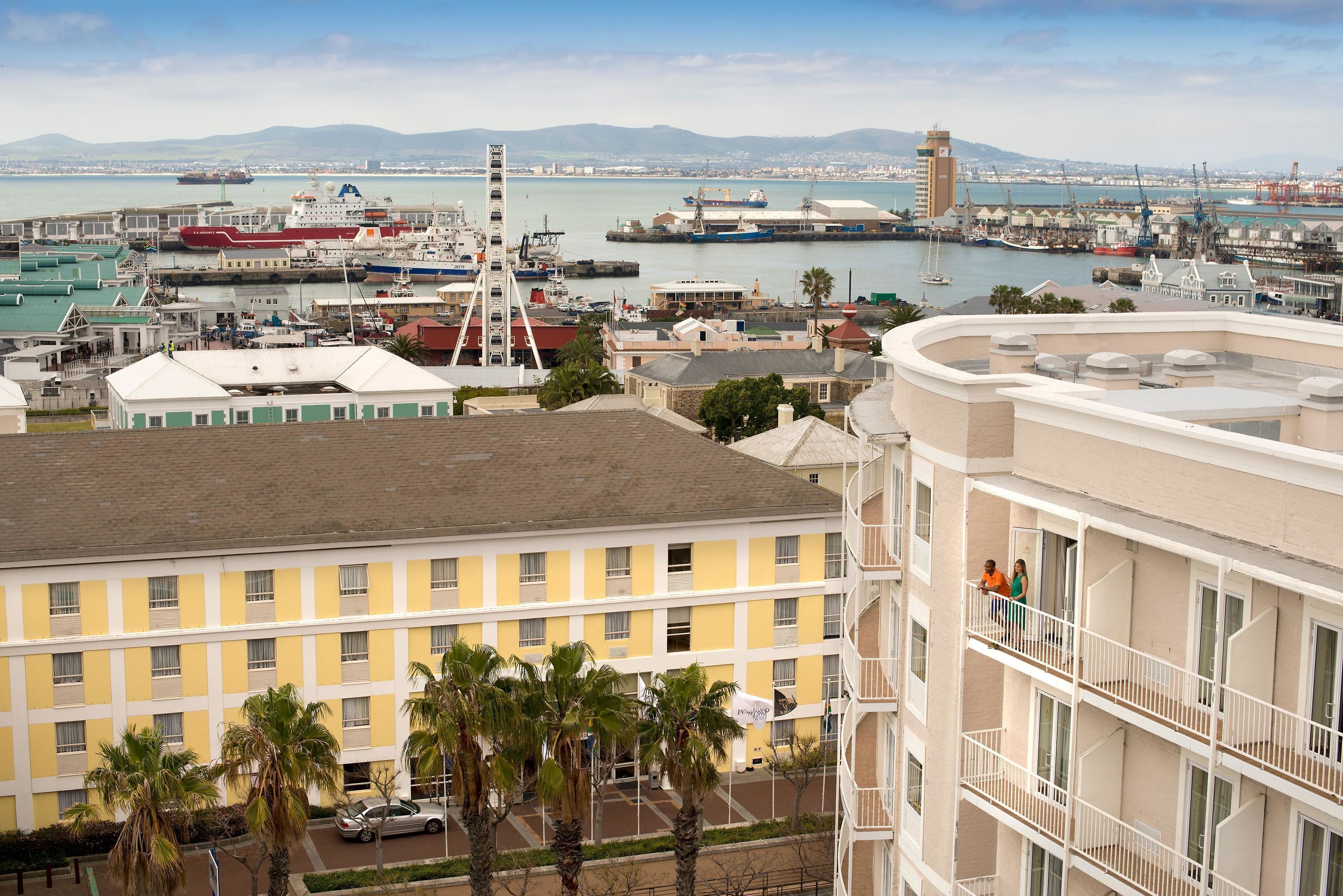 Un hotel moderno de gran altura con múltiples balcones que dan a un puerto deportivo con barcos y grúas.