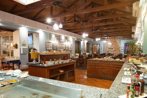 A restaurant with a buffet setup, wooden ceiling beams, and a stone wall.