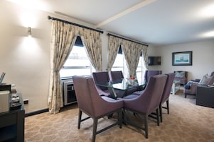 A dining area with a glass table and purple chairs, a sofa, and a TV on the wall.