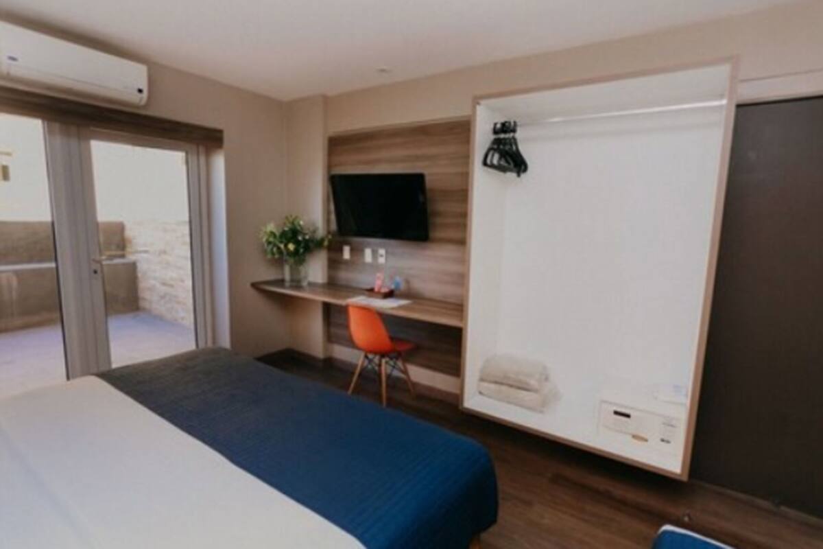 A hotel room with a bed, a desk with a chair, a television, and a sliding door.