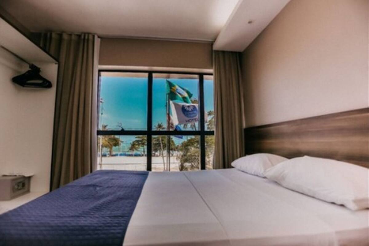 A hotel room with a large bed, a view of the beach, and a flag on the window.