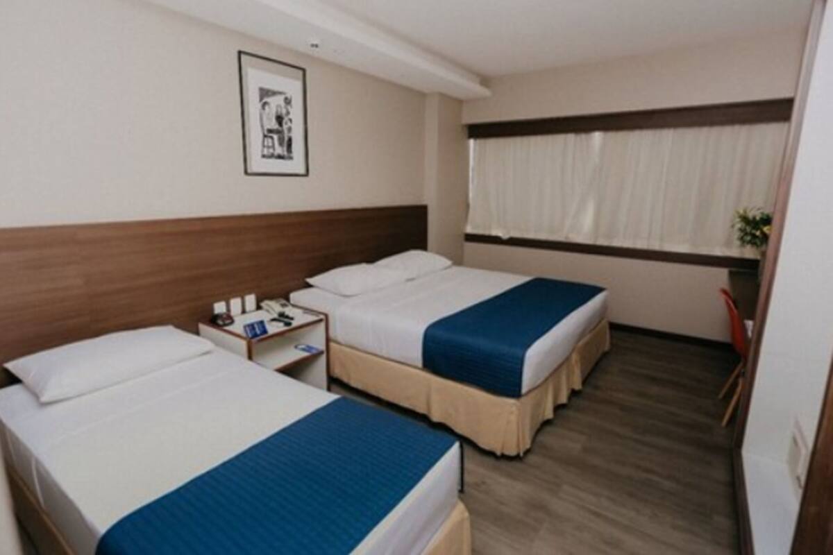 A hotel room with two beds, a nightstand, a window with curtains, and a framed picture on the wall.