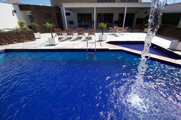 Una piscina con fuente acuática, rodeada de sillas de descanso y una terraza.