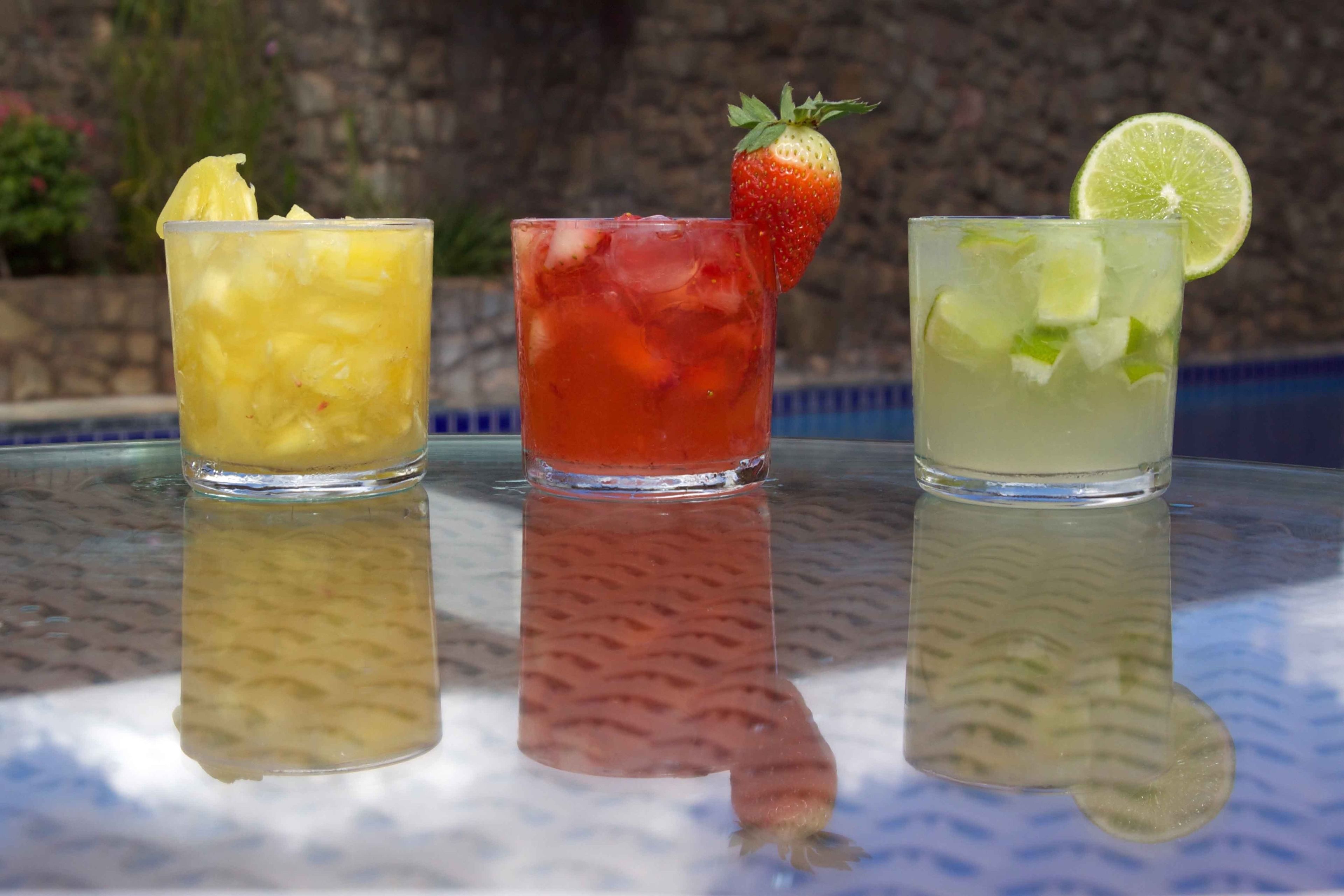 Three glasses of different beverages on a reflective surface.