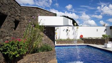 A swimming pool with a stone wall and a white building in the background.
