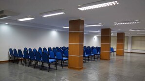 Un salón de conferencias con hileras de sillas azules, pilares de madera y suelo de baldosas.