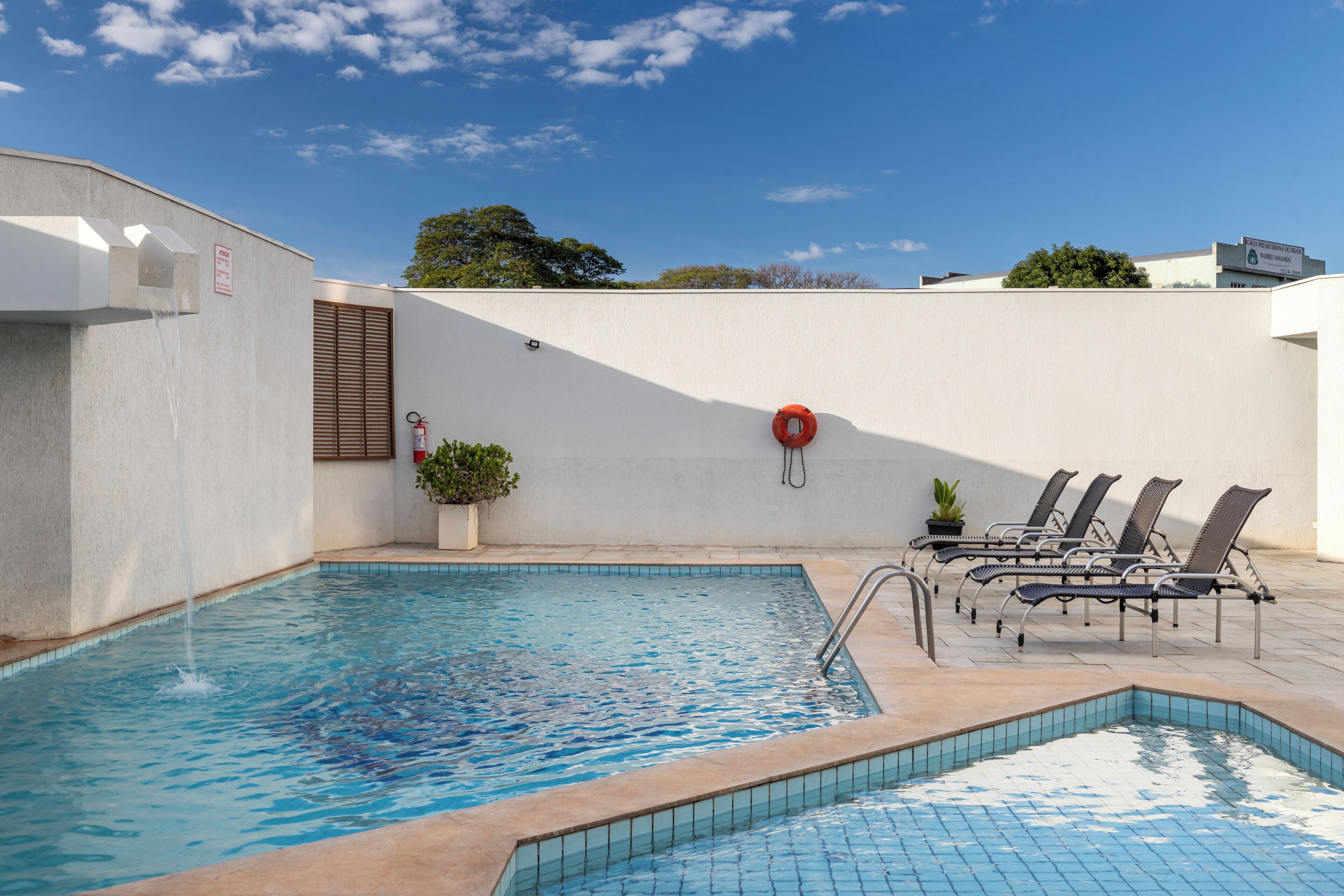 A swimming pool with a water fountain, lounge chairs, and a potted plant.