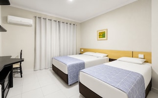 Una habitación de hotel con dos camas, un escritorio y una ventana con cortinas.