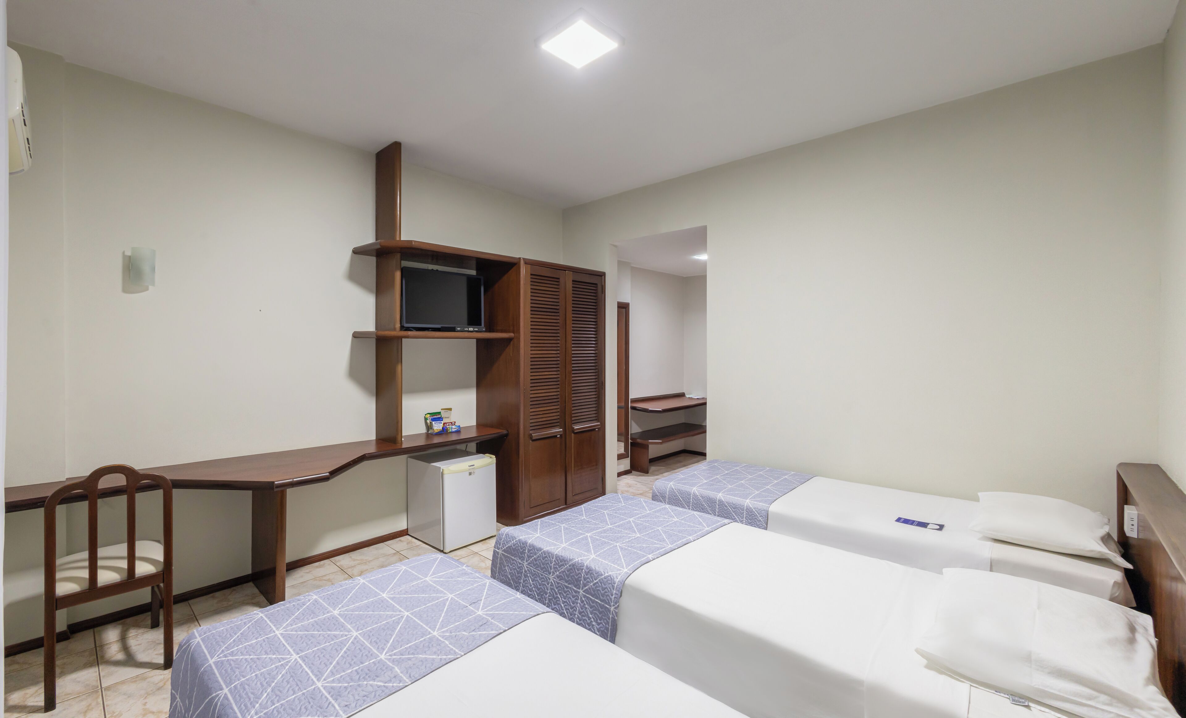 A hotel room with a desk, two beds, a wardrobe, and a television.