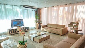 A living room with a beige sofa, a glass coffee table, a TV, and a potted plant.