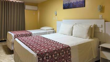 A hotel room with two beds, a large window with curtains, a wall-mounted air conditioner, and a geometric painting.
