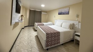 A hotel room with a bed, a bedside table, a TV mounted on the wall, a window with curtains, and a painting on the wall.
