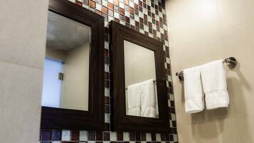 A bathroom with a white sink, two mirrors, a tiled wall, and a hanging light fixture.