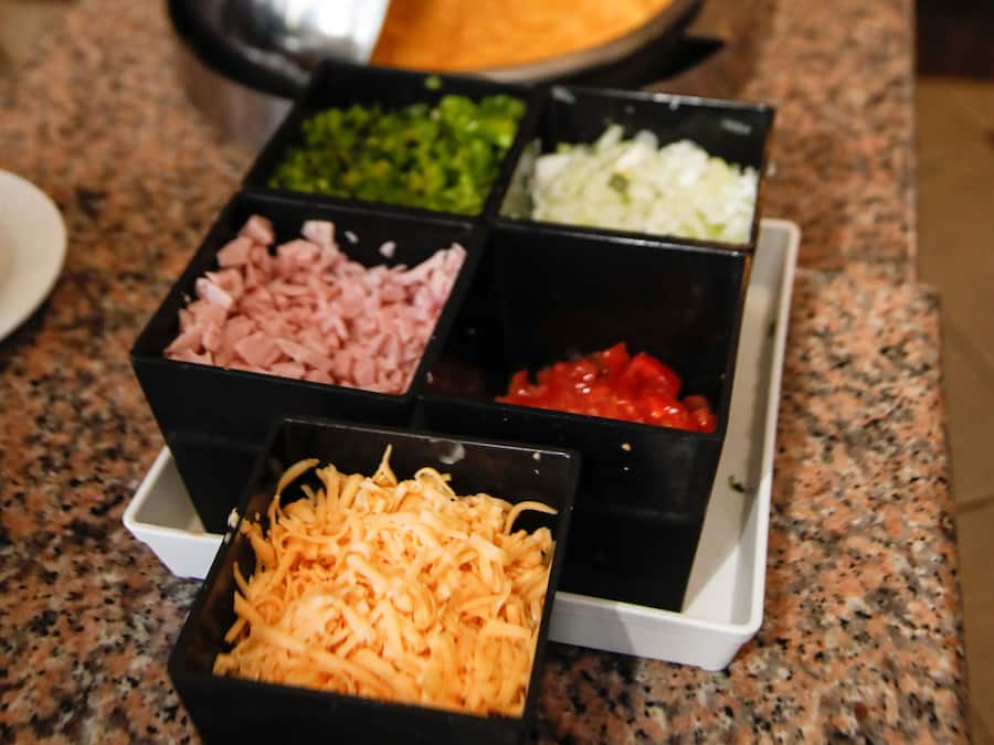 Un bufé con distintos alimentos en recipientes negros sobre una encimera de granito.