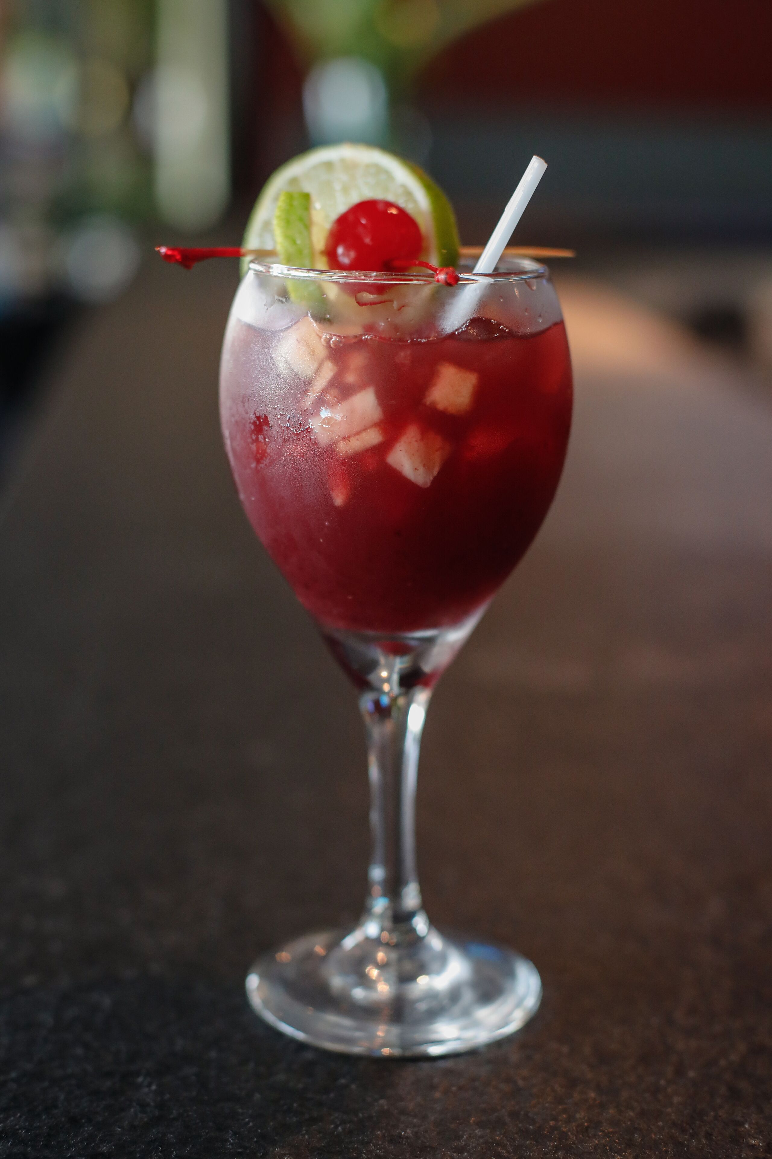 A cocktail in a stemmed glass with a lime wedge and a cherry garnish.