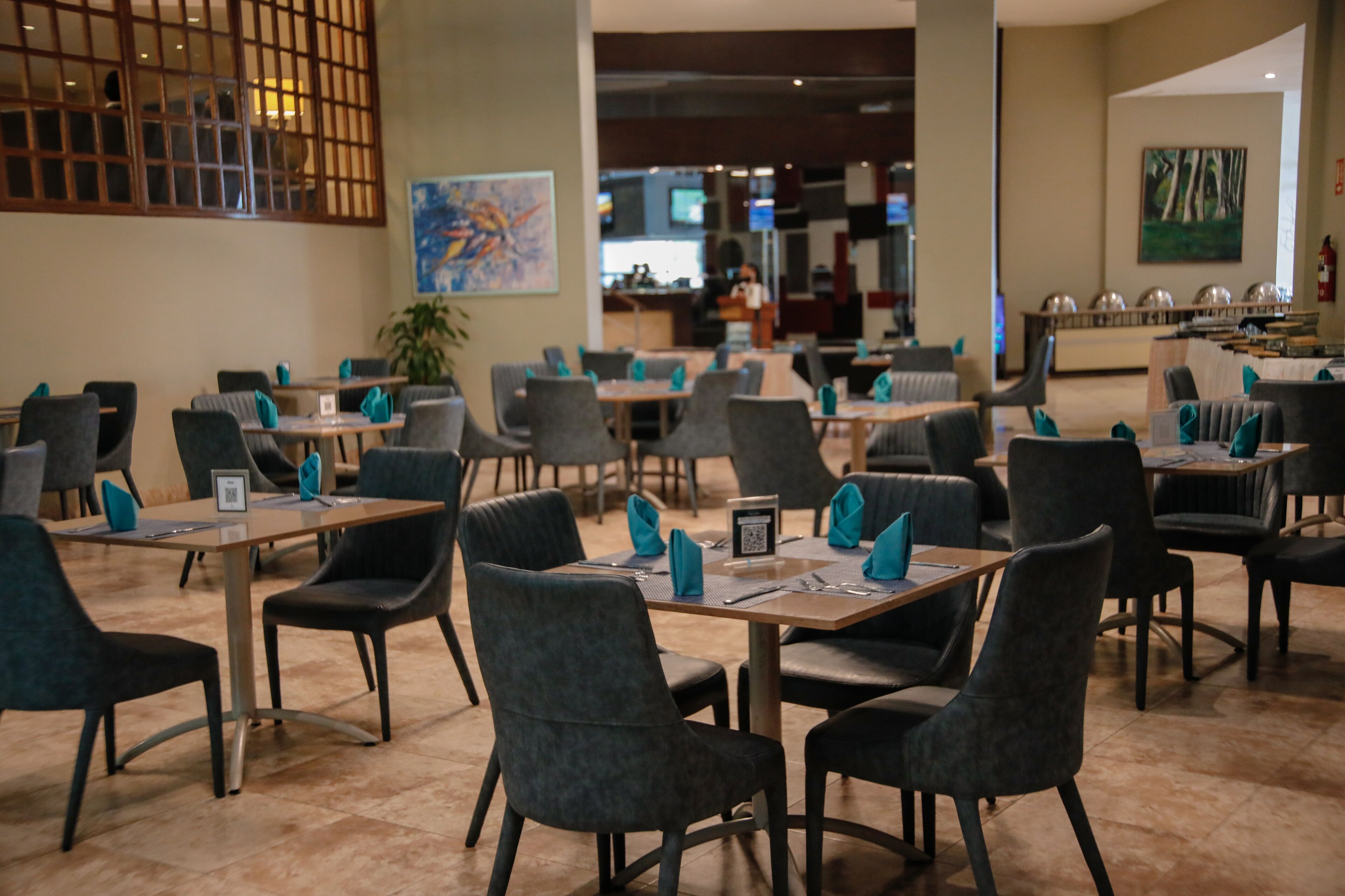 Un restaurante espacioso con varias mesas y sillas, una zona de bar al fondo y obras de arte en las paredes.