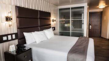 Une chambre d’hôtel avec un grand lit, une table de chevet avec un téléphone, une lampe fixée au mur et une porte coulissante.