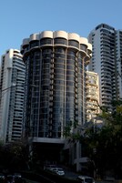 Un edificio moderno de gran altura con una sección central cilíndrica y varios balcones.