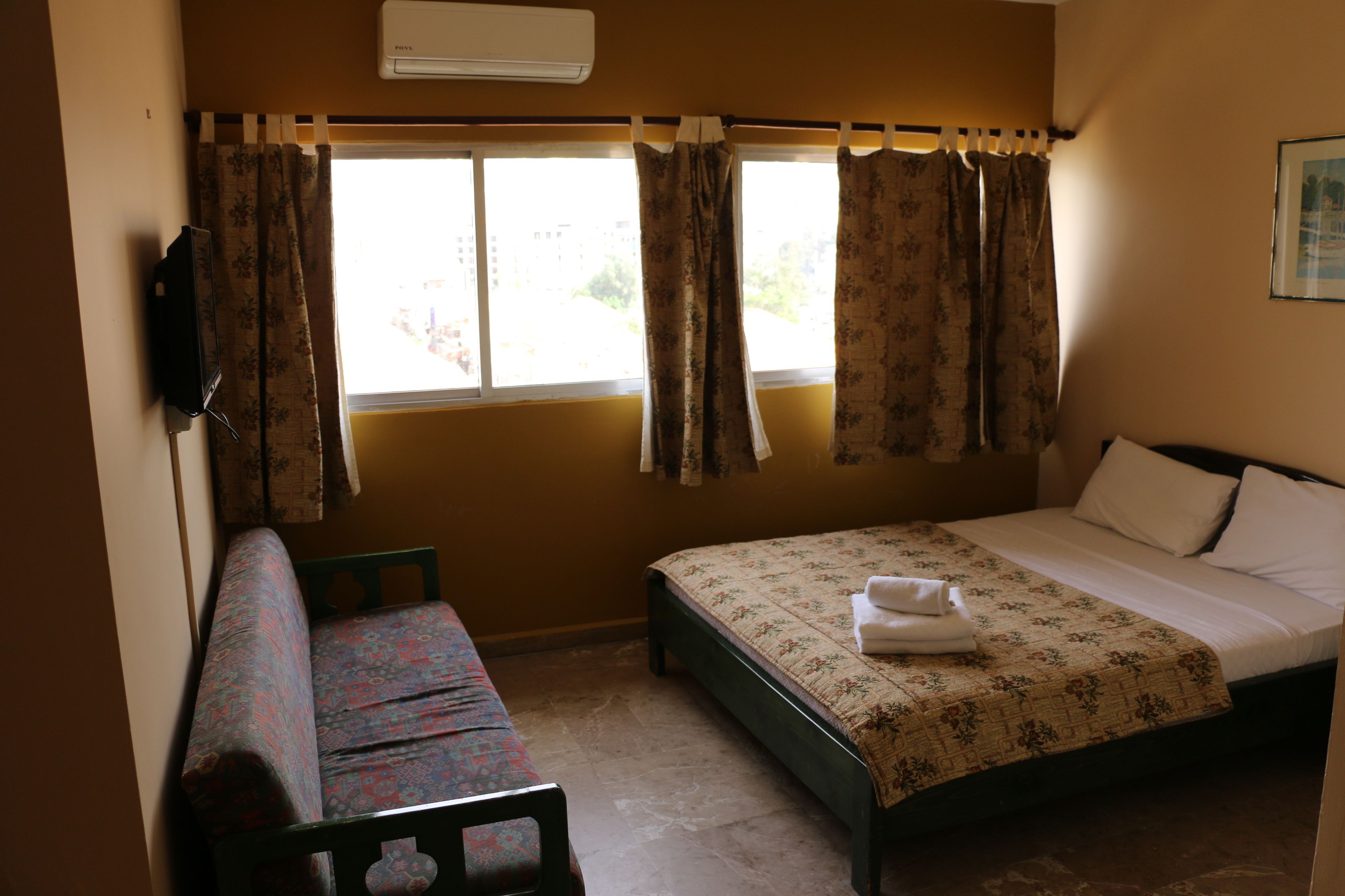 Un dormitorio con cama, una banca y una ventana con cortinas.