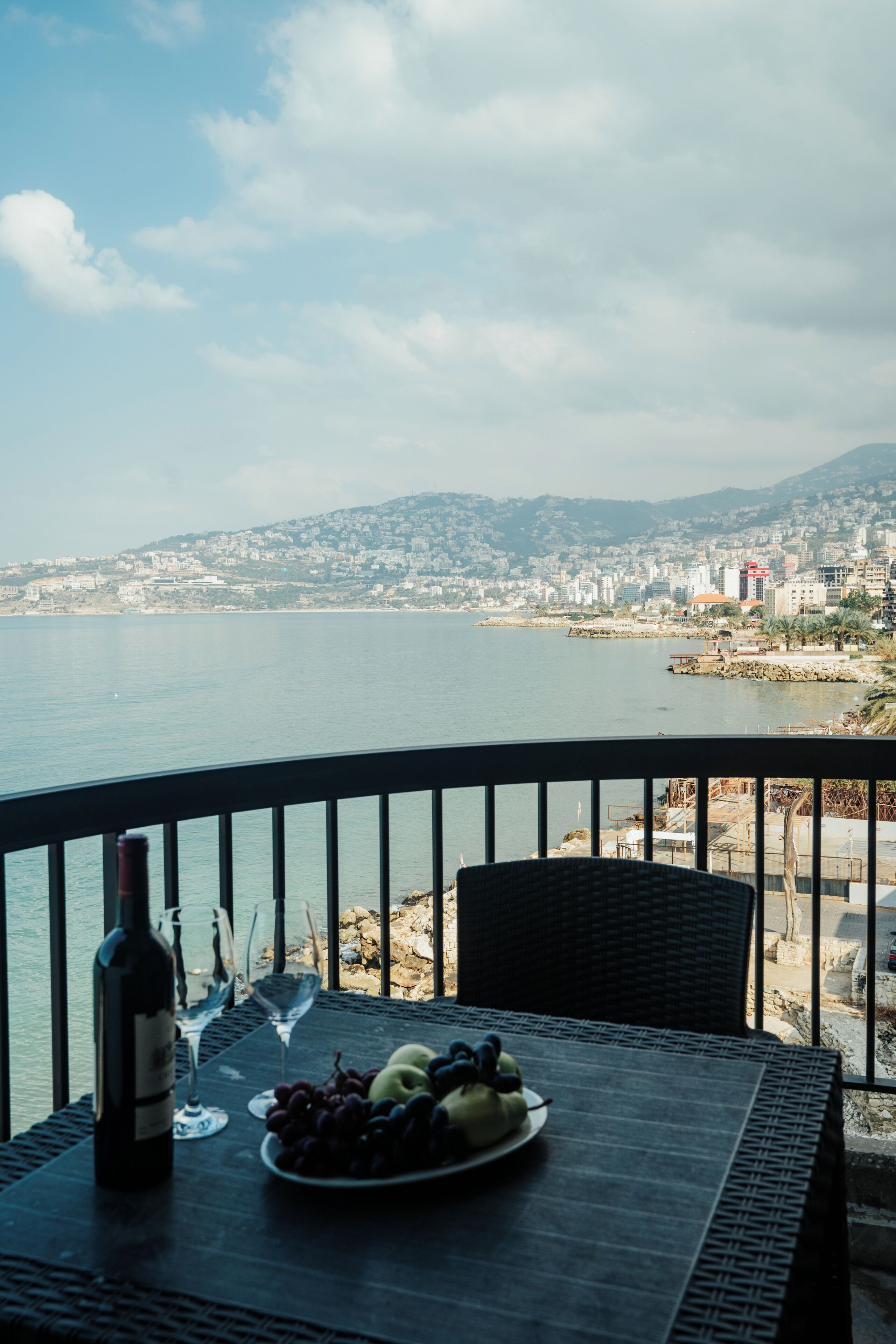 Un balcón con una mesa dispuesta para una comida, con vista a un paisaje urbano costero.
