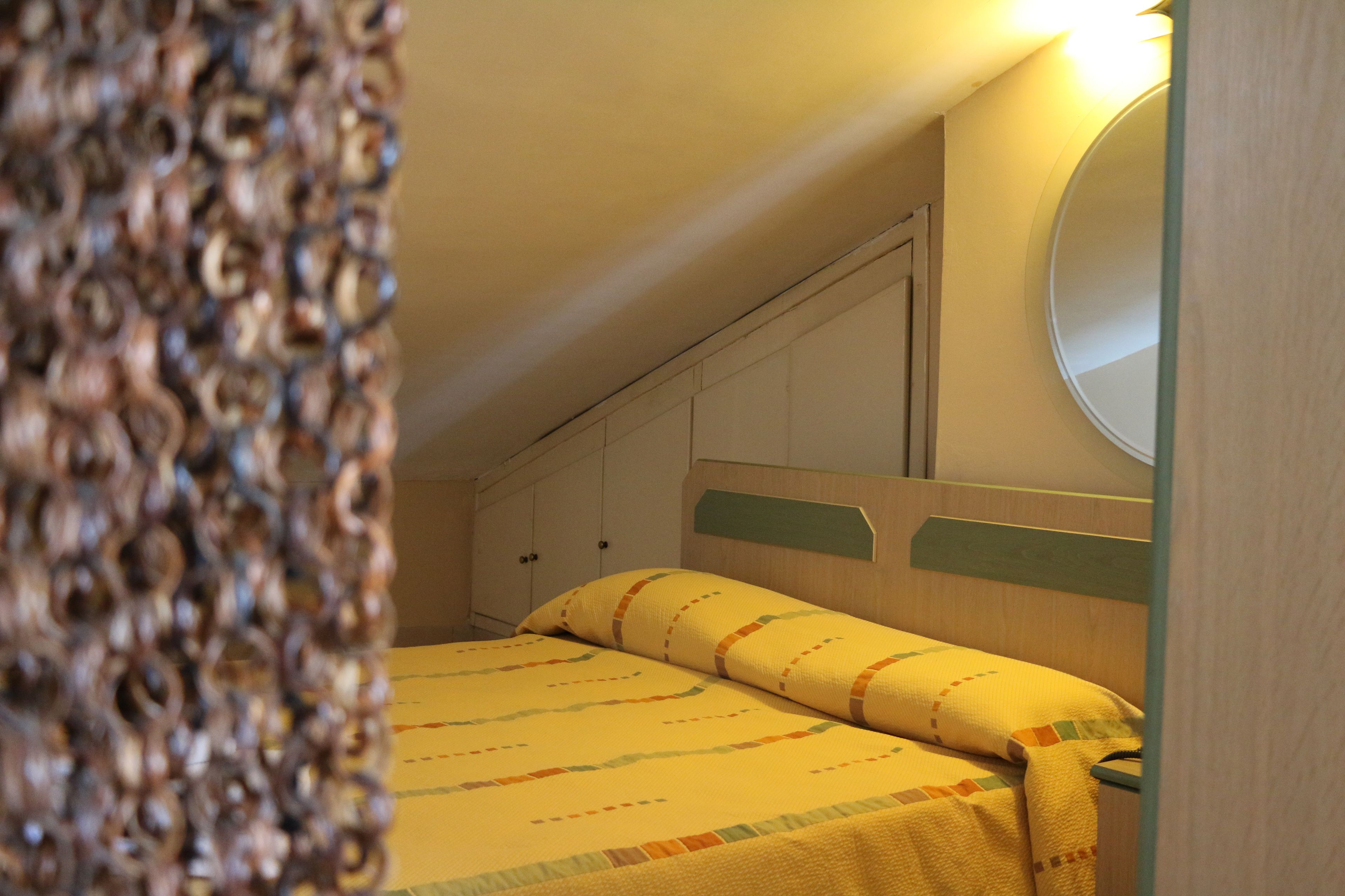 A bedroom with a bed, a wooden headboard, a wall-mounted mirror, and a wardrobe.