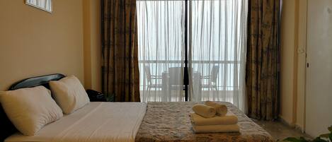 Habitación de hotel con cama, una mesita con toallas, una silla y un balcón con vistas.