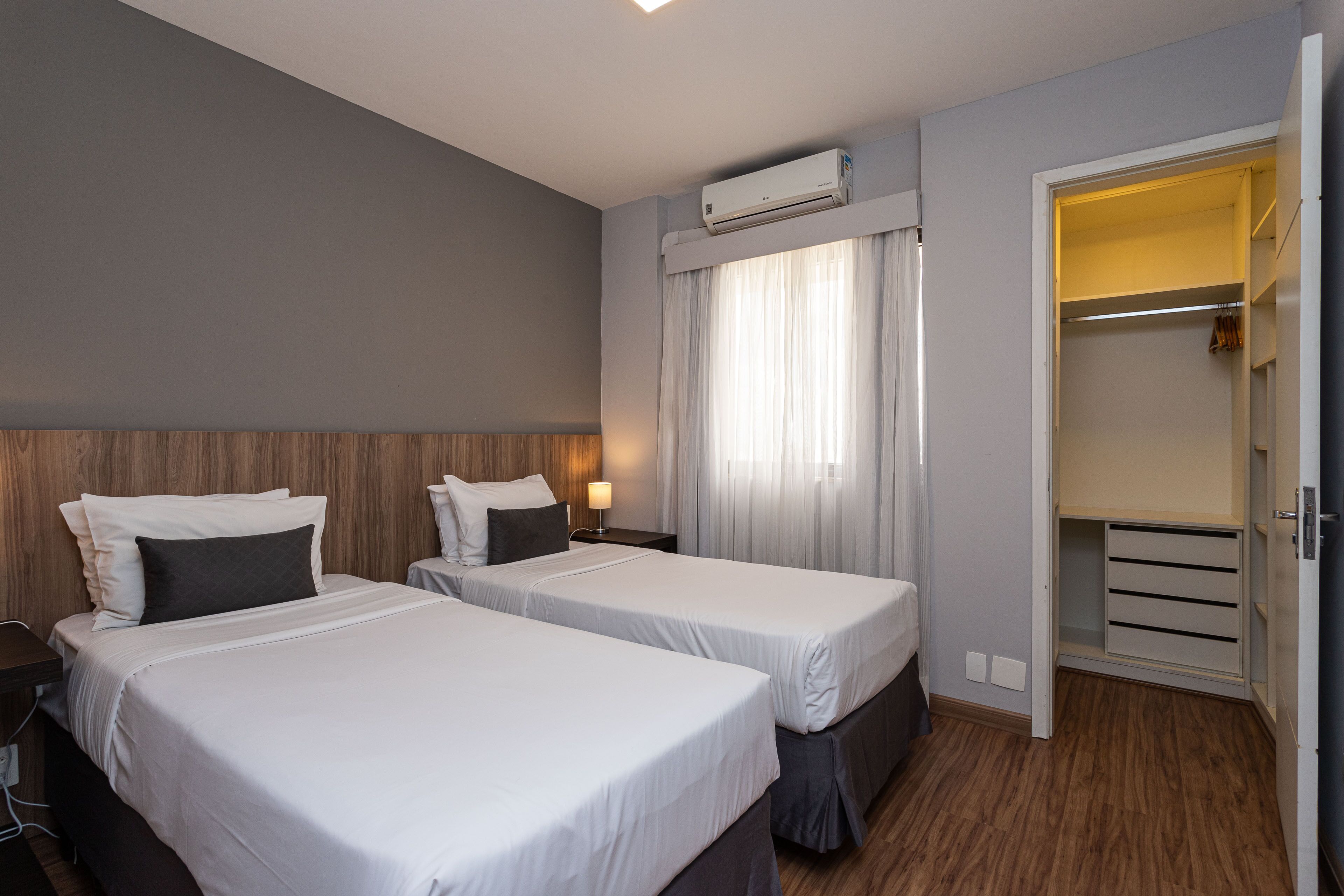A hotel room with two beds, a wardrobe, and an air conditioning unit.