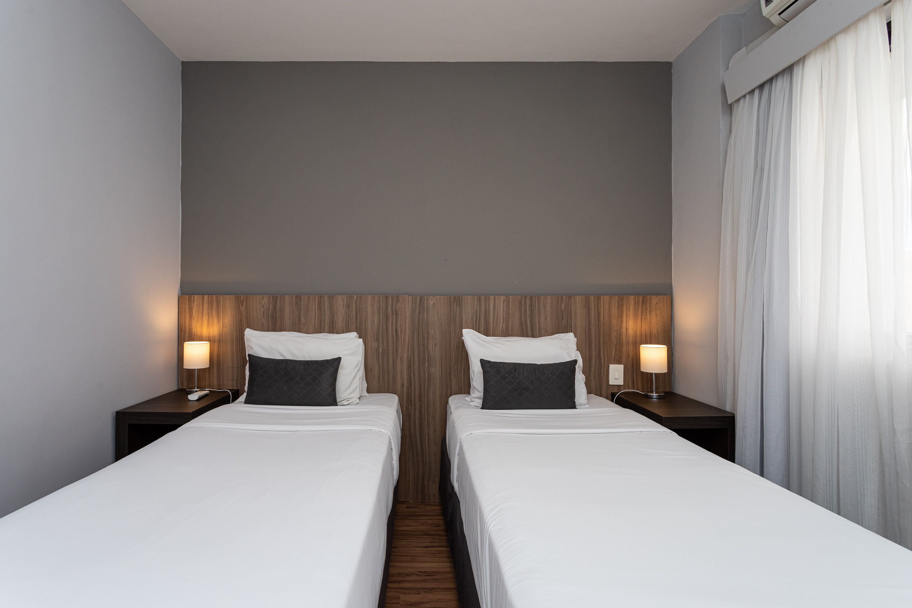 Habitación de hotel con dos camas, cabecero de madera, ropa de cama blanca y lámparas de noche.