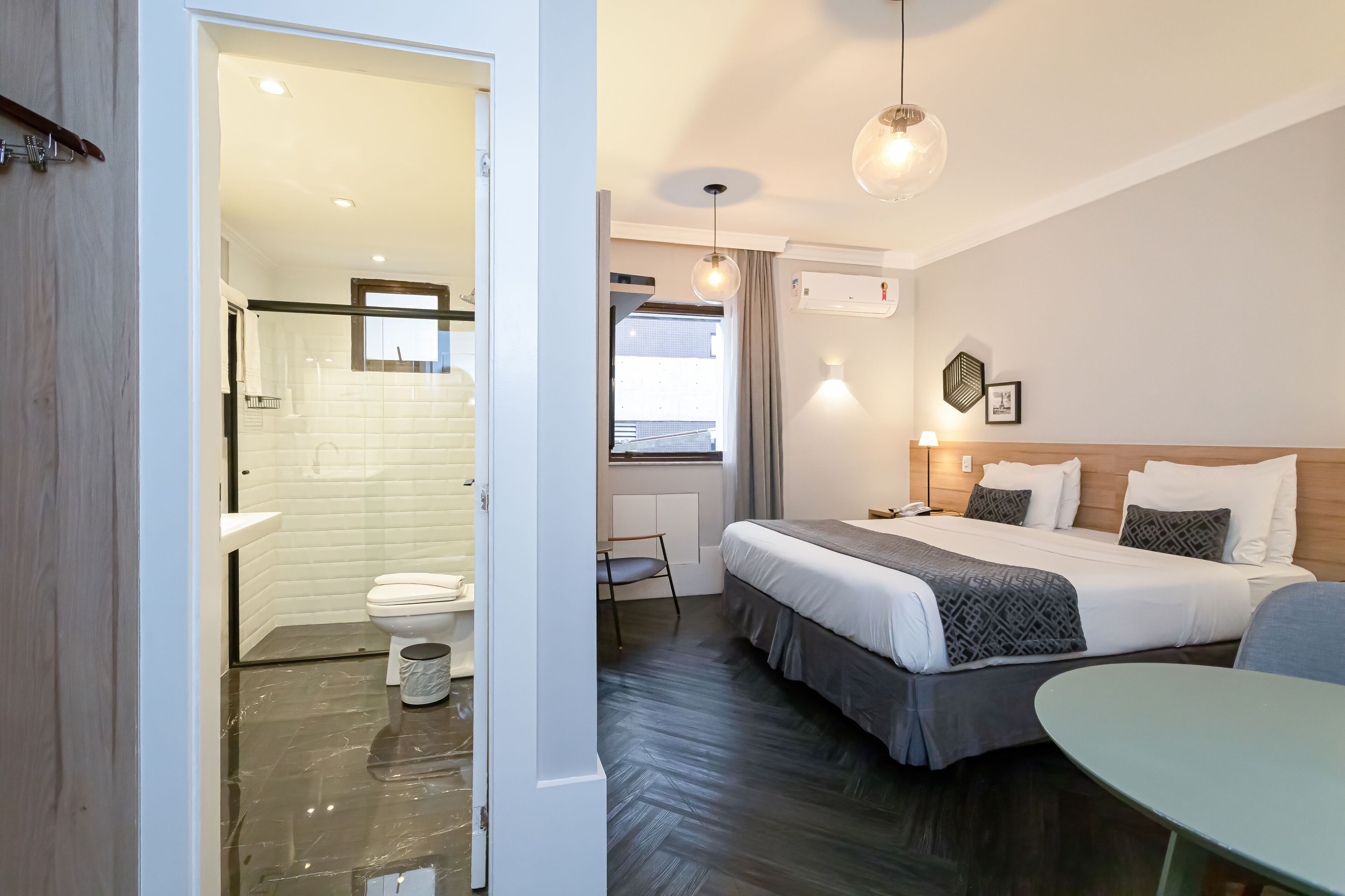 Et hotelværelse med en stor seng, et lille bord, et badeværelse med toilet og håndvask samt et vindue med gardiner.