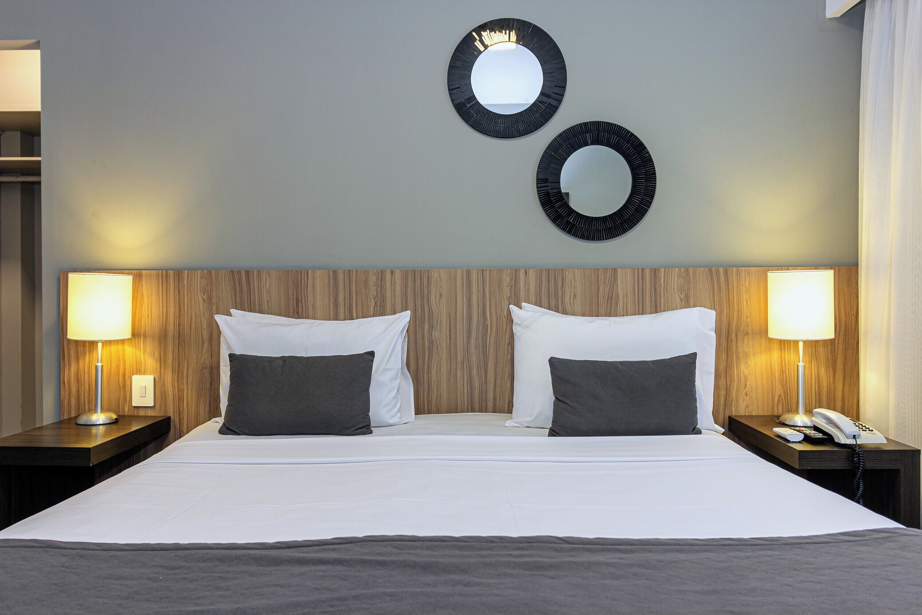 Une chambre d’hôtel avec un grand lit, deux lampes de chevet, un téléphone et deux miroirs fixés au mur.