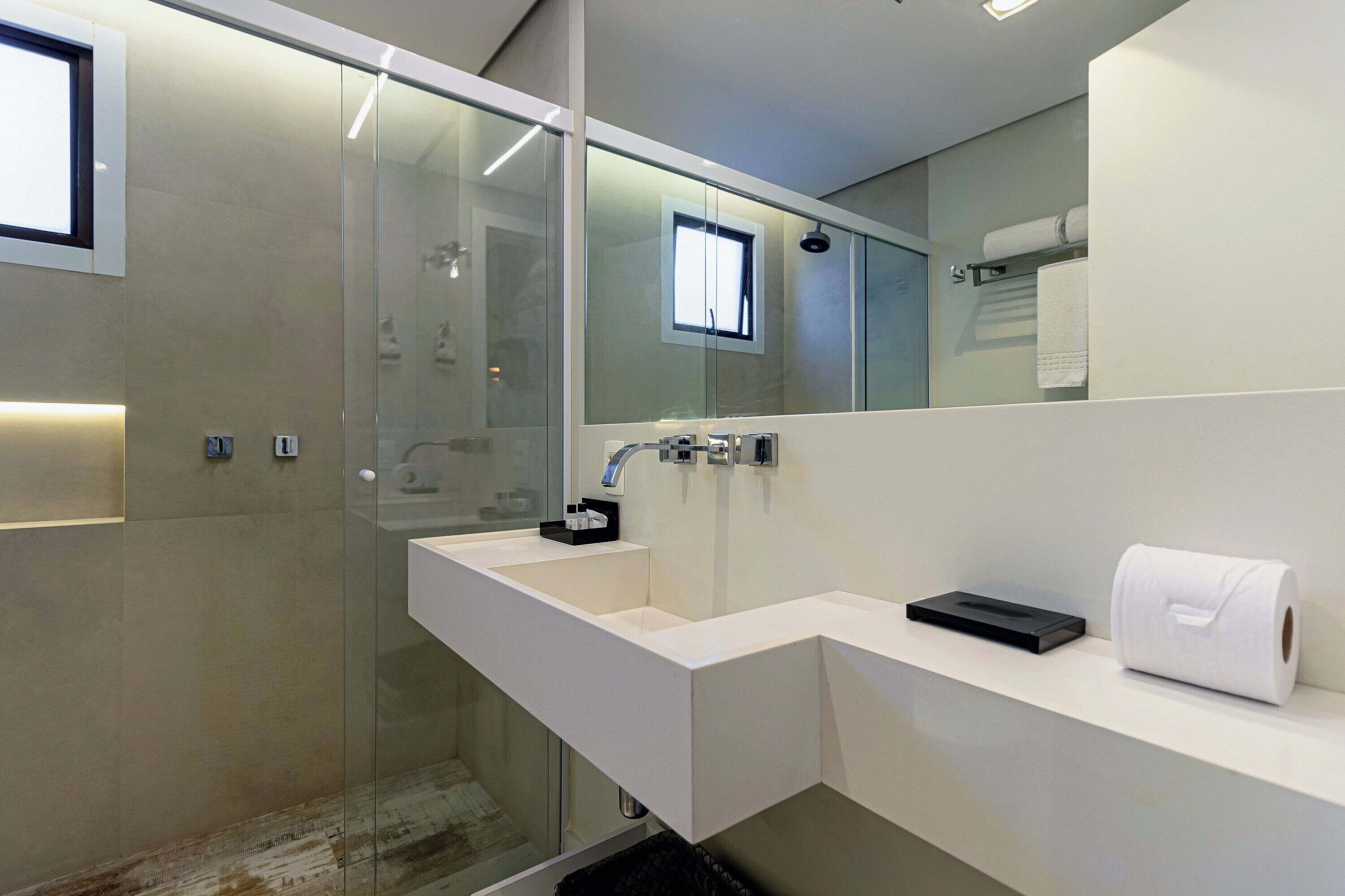 A modern bathroom with a glass shower enclosure, a white sink with a black soap dispenser, and a towel rack with a rolled towel.