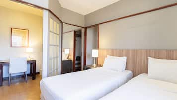 A hotel room with two beds, a desk, and a chair. There is a door leading to a closet and a staircase.