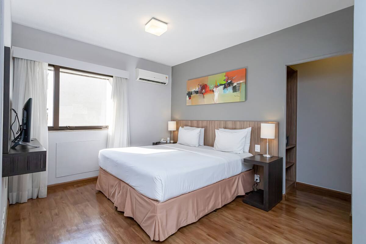 A hotel room with a large bed, bedside lamps, a flat-screen TV, and a window with curtains.