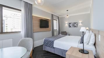 Habitación de hotel con cama, escritorio, silla, televisor montado en la pared y ventana con cortinas.