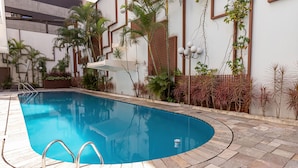 A swimming pool with a tiled deck, surrounded by various plants and a wooden fence. - H4 La Residence Paulista (São Paulo)
