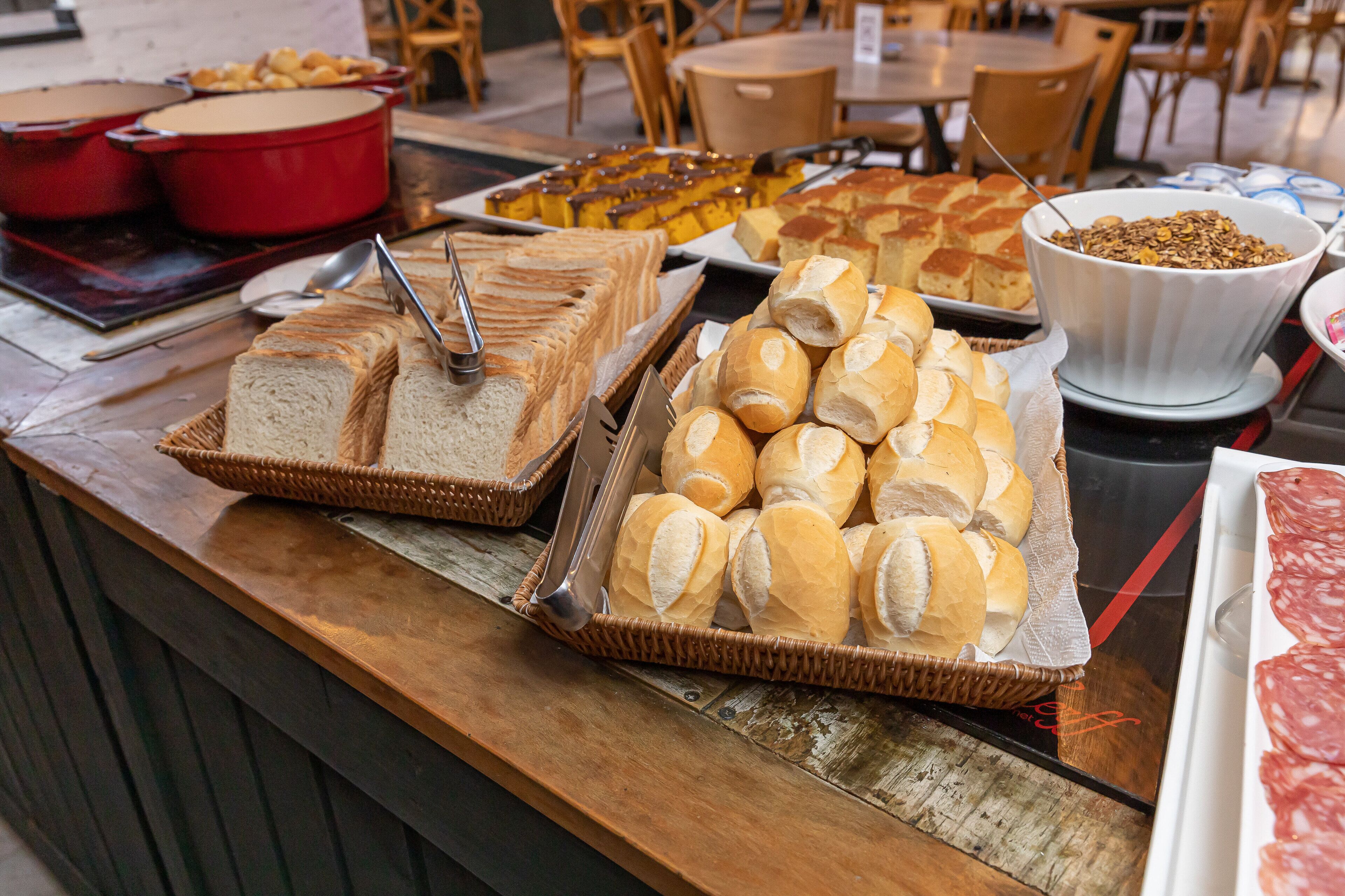 A buffet table with various food items including bread, pastries, and a bowl of granola.