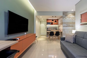 A modern living room with a flat-screen TV, a sofa, and a dining area with chairs.