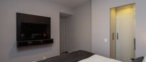 A modern hotel room with a large bed, a flat-screen TV mounted on the wall, and a wardrobe with a mirror.