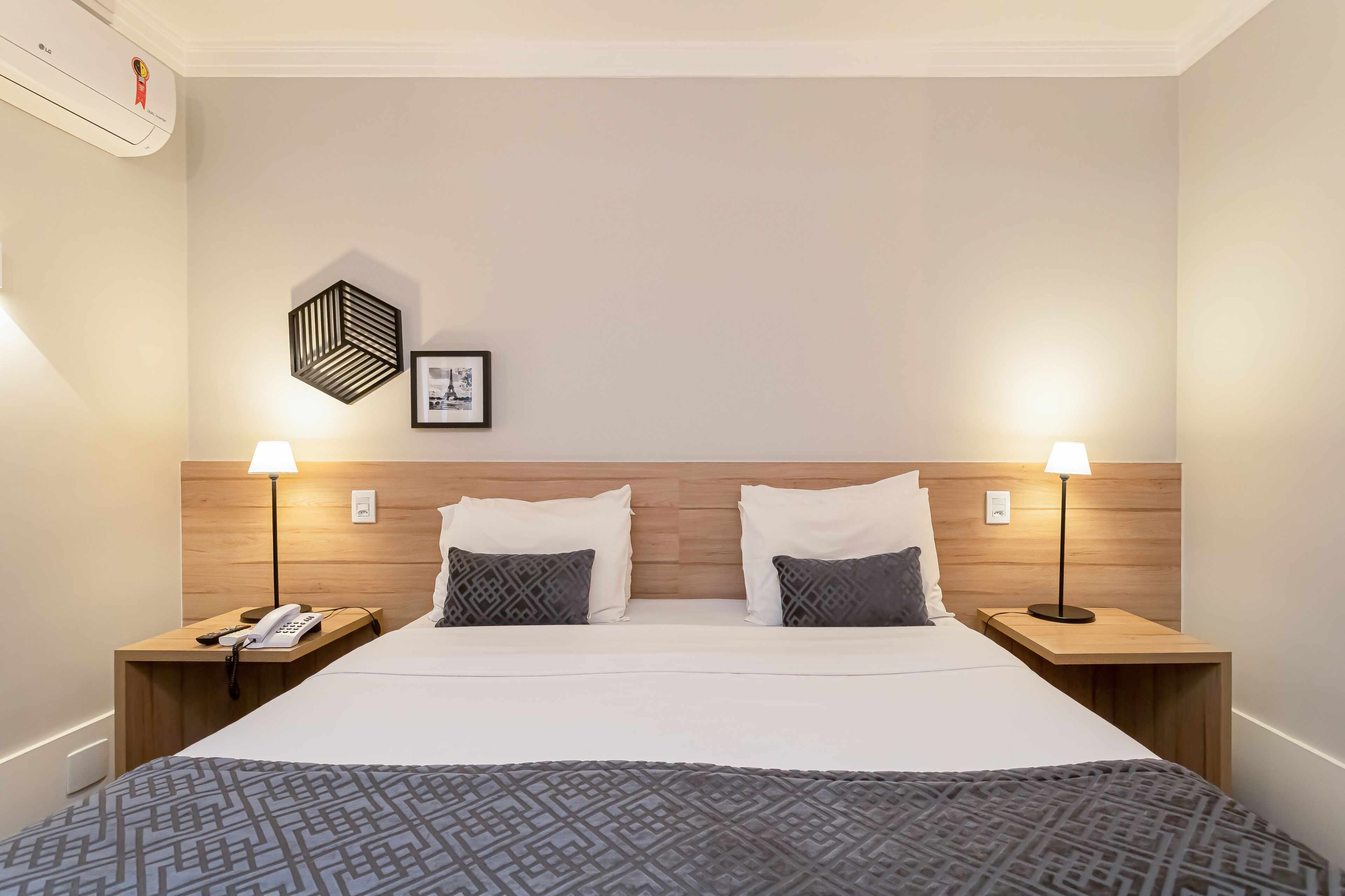 Une chambre d’hôtel avec un grand lit, deux tables de chevet avec des lampes, un téléphone et un tableau encadré au mur.