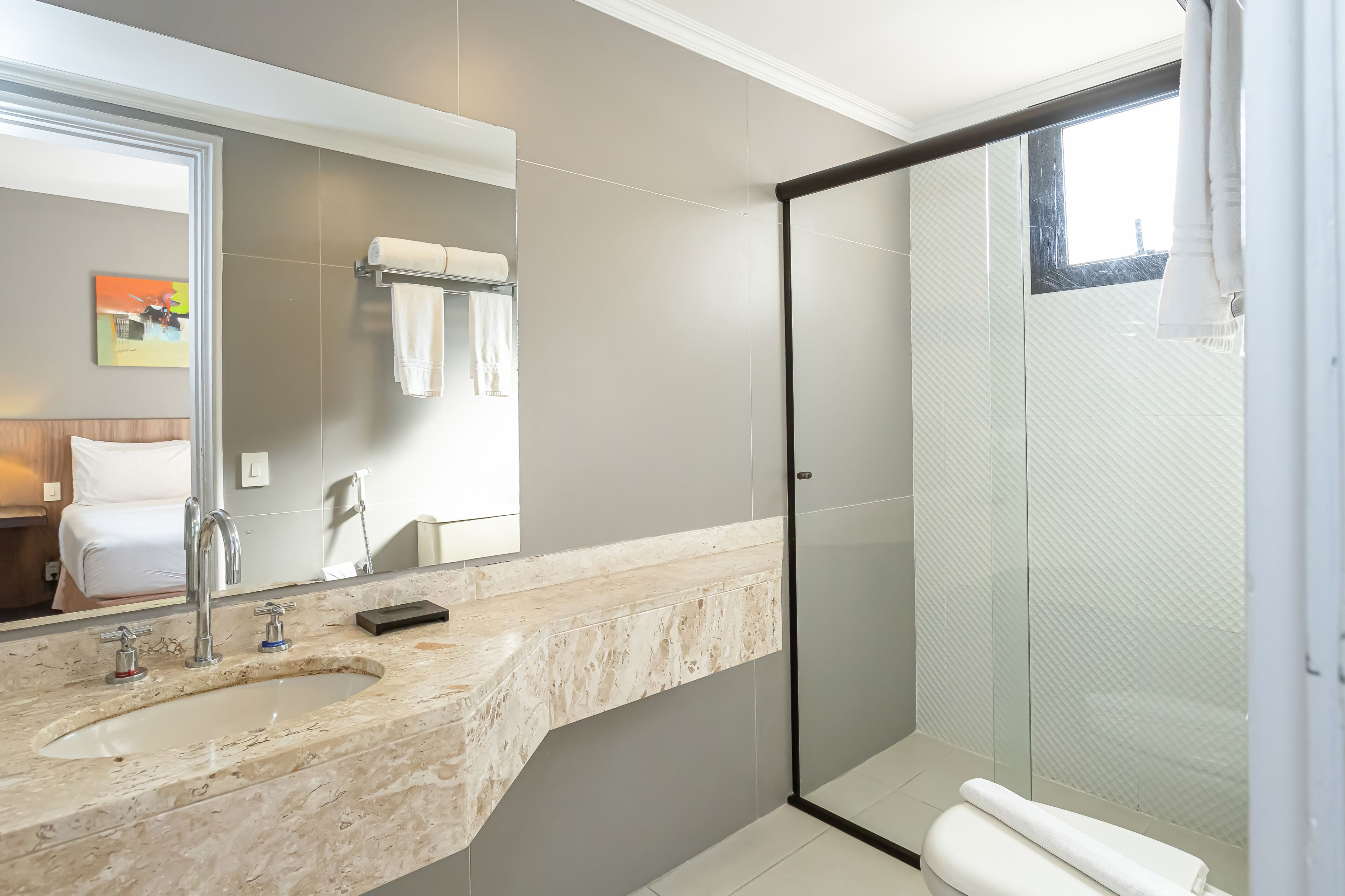Un baño moderno con un espejo grande, un lavabo de mármol y una ducha con mampara de vidrio.